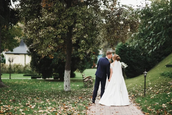 結婚式の日に公園を歩く幸せな新婚旅行のスタイリッシュなカップル花束 — ストック写真