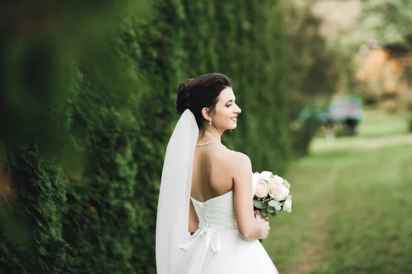 Bela noiva em elegante vestido branco segurando buquê posando no parque — Fotografia de Stock