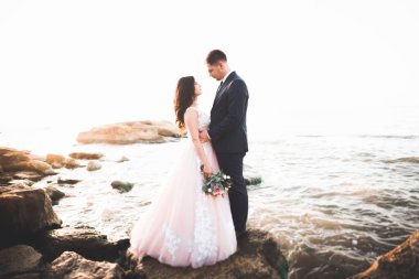 Düğün çifti, damat, gelin deniz kenarında ve mavi gökyüzünde poz veriyor.