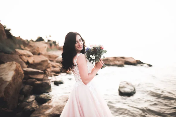 Bella dama, novia posando en un vestido de novia cerca del mar al atardecer —  Fotos de Stock
