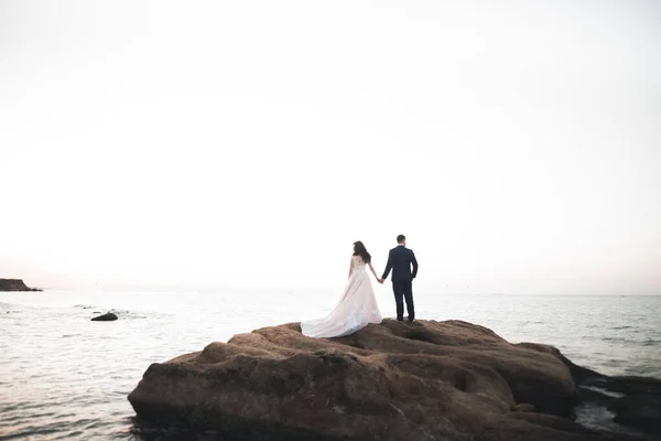 Wedding couple kissing and hugging on rocks near blue sea — Stock Photo, Image