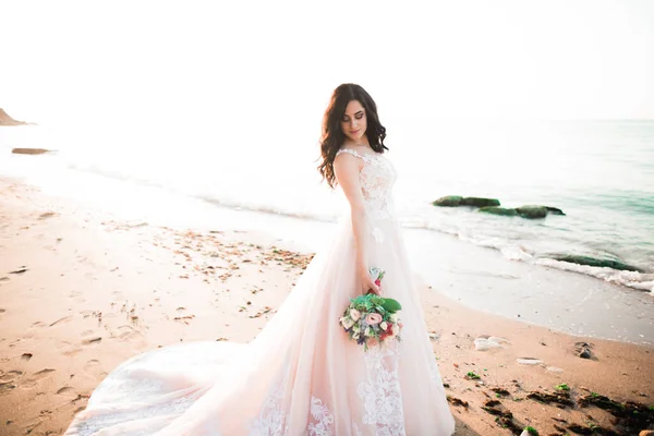 Bella dama, novia posando en un vestido de novia cerca del mar al atardecer —  Fotos de Stock