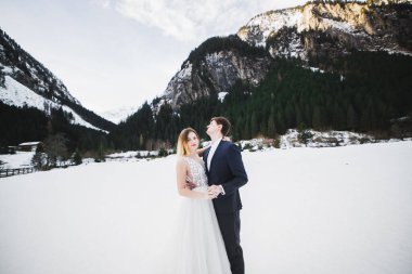 Kış dağlarında güzel genç bir çift. Aşıkların kış yürüyüşü. Erkek kadına sarılıyor.