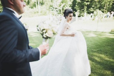 Romantik, peri masalı, mutlu yeni evli çift parkta sarılıp öpüşüyor, arka planda ağaçlar...