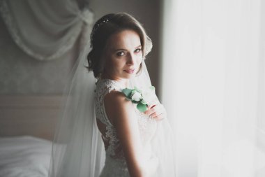 Cüppeli muhteşem gelin bir odada düğün töreni için poz veriyor ve hazırlanıyor.