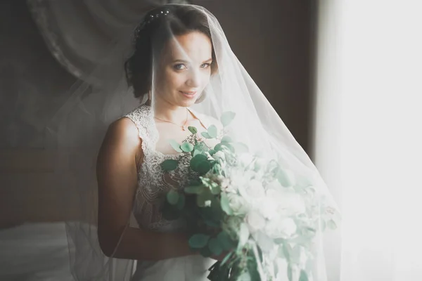 Preciosa novia en bata posando y preparándose para la ceremonia de boda cara en una habitación — Foto de Stock