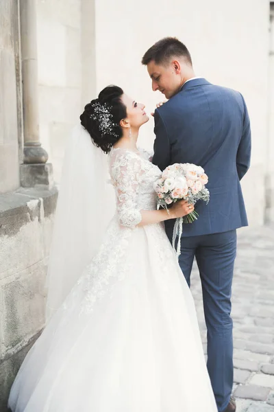 Krásný šťastný svatební pár, nevěsta s dlouhými bílými šaty pózuje v krásném městě — Stock fotografie