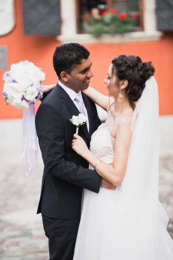 Düğün fotoğrafı çekimi. Gelin ve damat şehirde yürüyorlar. Birbirlerine sarılıp bakan evli bir çift. Tutma buketi