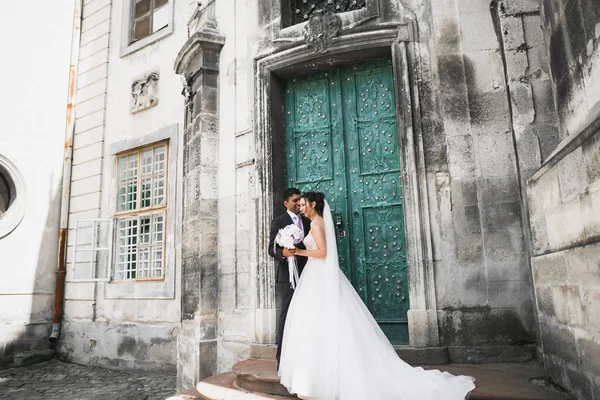 Szép boldog házaspár, menyasszony hosszú fehér ruha pózol a gyönyörű városban — Stock Fotó