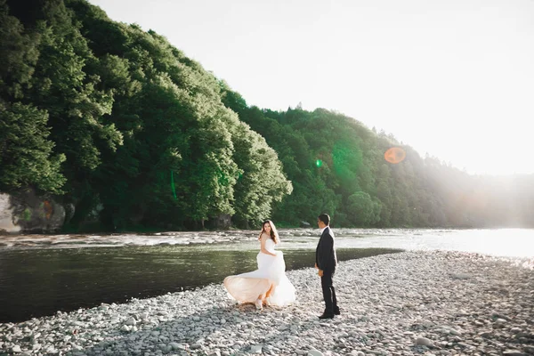 Elegante novia rubia feliz y elegante novio en el fondo de un hermoso río en las montañas —  Fotos de Stock