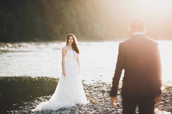 Elegáns elegáns, boldog szőke menyasszony és gyönyörű vőlegény a háttérben egy gyönyörű folyó a hegyekben — Stock Fotó
