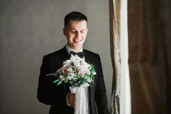 Piękny mężczyzna, pan młody trzyma duży i piękny bukiet ślubny z kwiatami — Zdjęcie stockowe