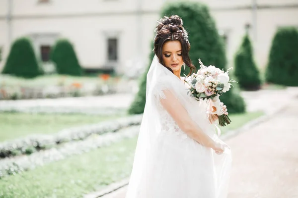 Hermosa novia en elegante vestido blanco sosteniendo ramo posando en el parque — Foto de Stock