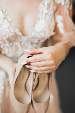 Zarif beyaz elbiseli güzel gelin ellerinde düğün ayakkabıları tutuyor.