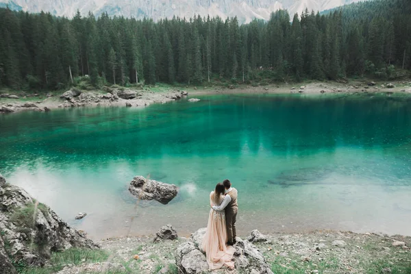 Matrimonio coppia sulla natura si sta abbracciando vicino a un bellissimo lago in montagna.. Bella ragazza modello in abito bianco. Uomo in completo — Foto Stock