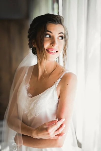 Preciosa novia en bata posando y preparándose para la ceremonia de boda cara en una habitación —  Fotos de Stock