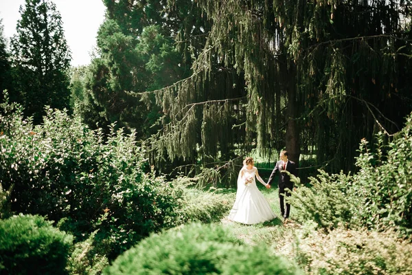 結婚式の日に公園を歩く幸せな新婚旅行のスタイリッシュなカップル花束 — ストック写真