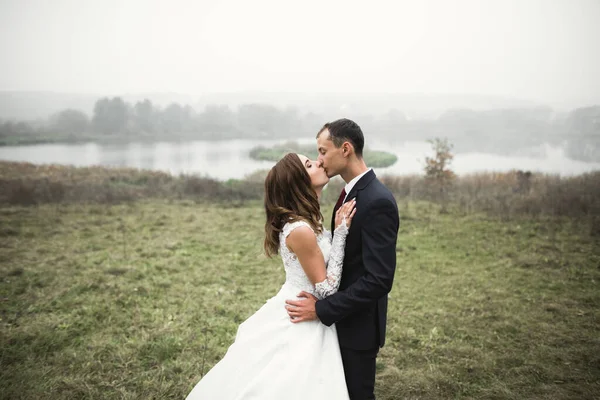 Romántico, cuento de hadas, feliz pareja recién casada abrazándose y besándose en un parque, árboles en el fondo — Foto de Stock