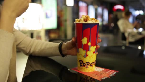 Dziewczyna siedzi w Cafe przed film i jedzenia Popcorn — Wideo stockowe