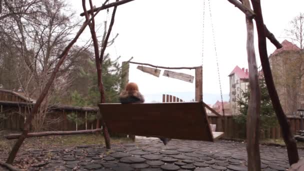 Девочка ранней весной качается на деревянном качеле — стоковое видео