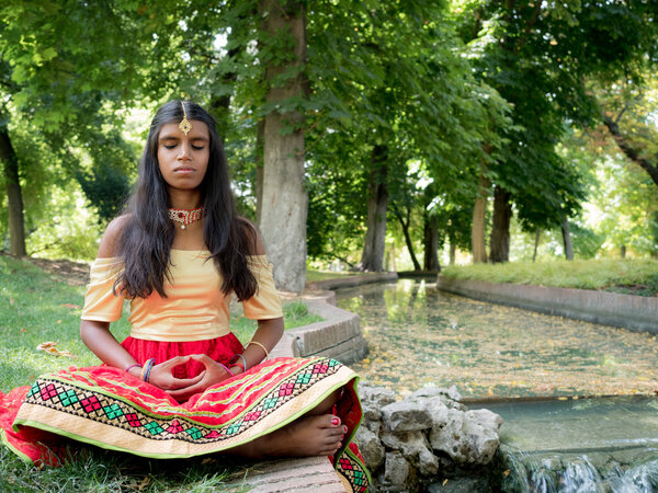 Красивая молодая индианка, практикующая медитацию в парке
