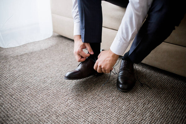 man ties the laces in his shoes in the morning in the room