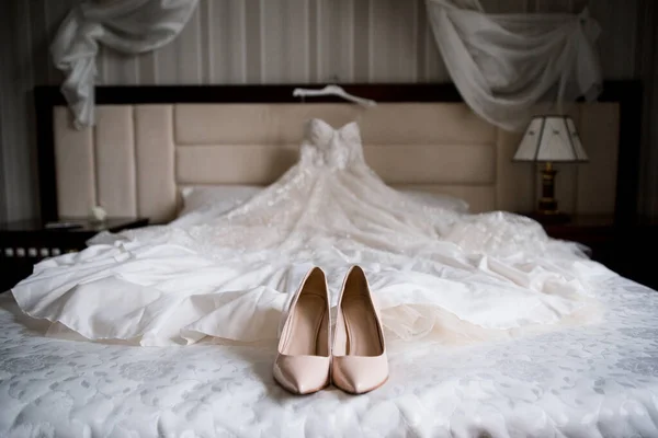 a bride\'s wedding shoes and wedding dress on the bed