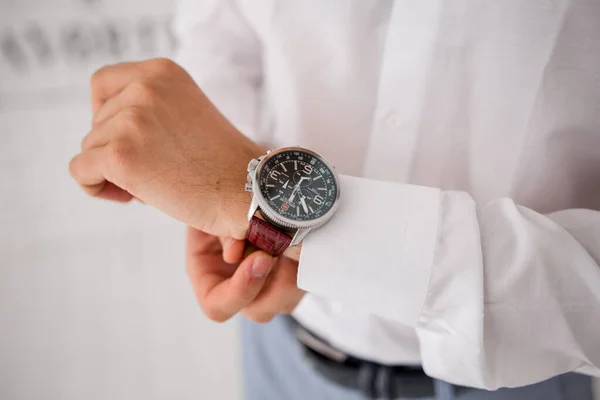 man puts a watch on his hand in a suit