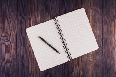 Ahşap masanın üzerinde kalem olan bir defter.