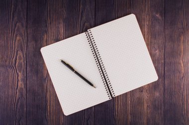 Ahşap masanın üzerinde kalem olan bir defter.