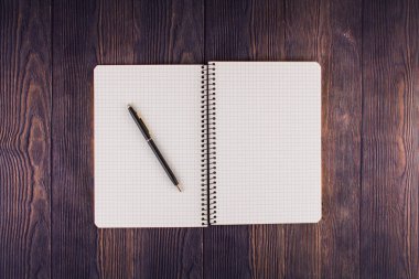 Ahşap masanın üzerinde kalem olan bir defter.