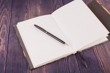 Ahşap masanın üzerinde kalem olan bir defter.