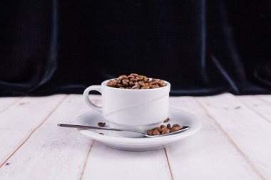 Tahta bir masada beyaz bir fincanda kahve çekirdeği.