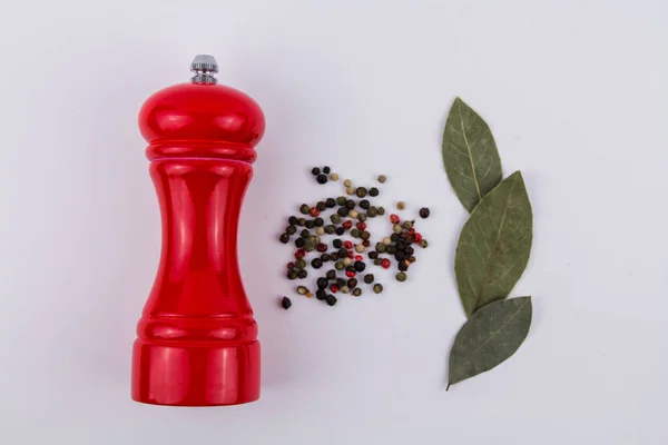 a pepper shaker with peppercorns and bay leaves on a white background