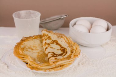 Mutfak masasının üzerinde un, çırpı ve yumurta dolu yuvarlak, güzel bir krep.