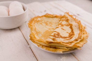 İnce, leziz yuvarlak krepler beyaz bir tabakta, ahşap masada, mutfakta yumurta ve un ile.