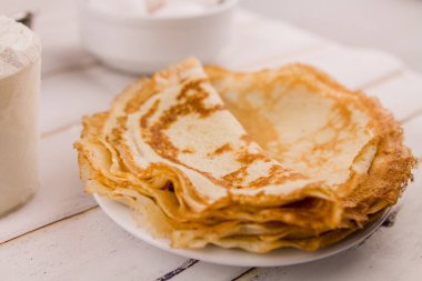 İnce, leziz yuvarlak krepler beyaz bir tabakta, ahşap masada, mutfakta yumurta ve un ile.