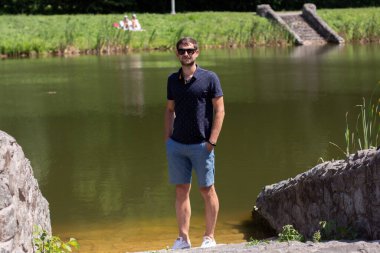 Yazın göl kenarında gözlüklü ve şortlu bir adam.