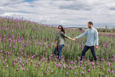 Yazın açık havada elinde çiçeklerle parkta yürüyen bir kadınla bir adam.