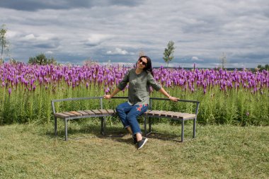 Koyu saçlı kız yazın mor çiçeklerle dolu bir tarlada oturuyor.