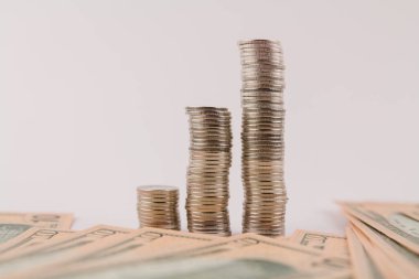 Beyaz arka planda dolar banknotlarıyla sütunlar halinde para sikkeleri