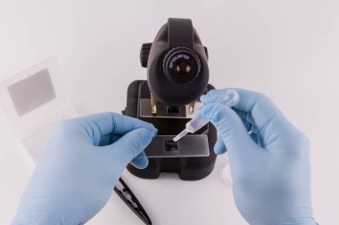 Mavi eldivenli bir laboratuar asistanı mikroskop ile çalışıyor.