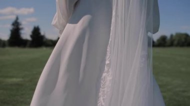 Gelinlik giymiş bir gelin yeşil çimlerle bir tarlada yürüyor.