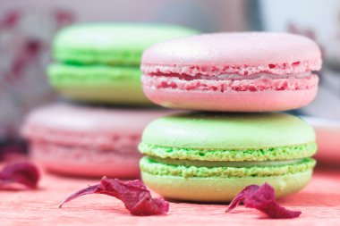 Yığılmış, lezzetli pembe ve yeşil Macaroons, renkli lezzetli Fransız hamur işleri, çilek ve fıstık macaroons pembe kağıt arka plan üzerinde kuru Şakayık yaprakları ile dekore edilmiş.