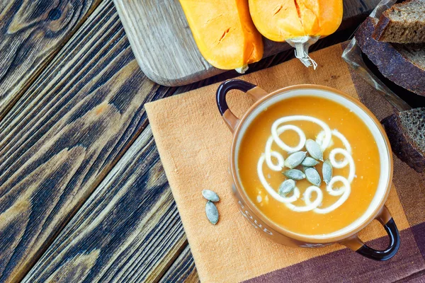 Geröstete Kürbissuppe mit Sahne, frischen Kürbissen und Kürbiskernen im Teller auf Holzgrund. Kopierraum — Stockfoto