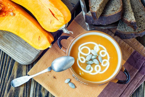 Geröstete Kürbissuppe mit Sahne, frischen Kürbissen und Kürbiskernen im Teller auf Holzgrund. Kopierraum — Stockfoto