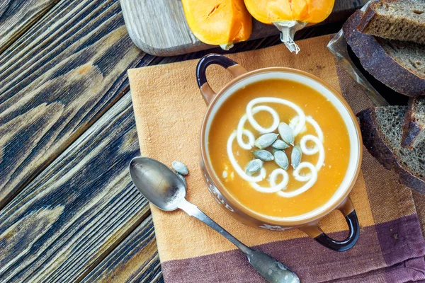 Geröstete Kürbissuppe mit Sahne, frischen Kürbissen und Kürbiskernen im Teller auf Holzgrund. Kopierraum — Stockfoto