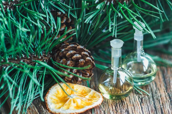 Aceite esencial en botella de vidrio con piñas, naranjas y ramas de abeto sobre fondo de madera — Foto de Stock