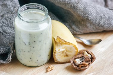 Sağlıklı bir sabah yemeği için cam kavanozda muz ve fındıklı yoğurt, seçici odaklanma.