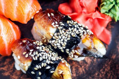 Suşi Seti sashimi ve suşi rulo koyu plaka üzerinde servis edilir. Koyu arka plan üzerinde Japon gıda görüntüsü.